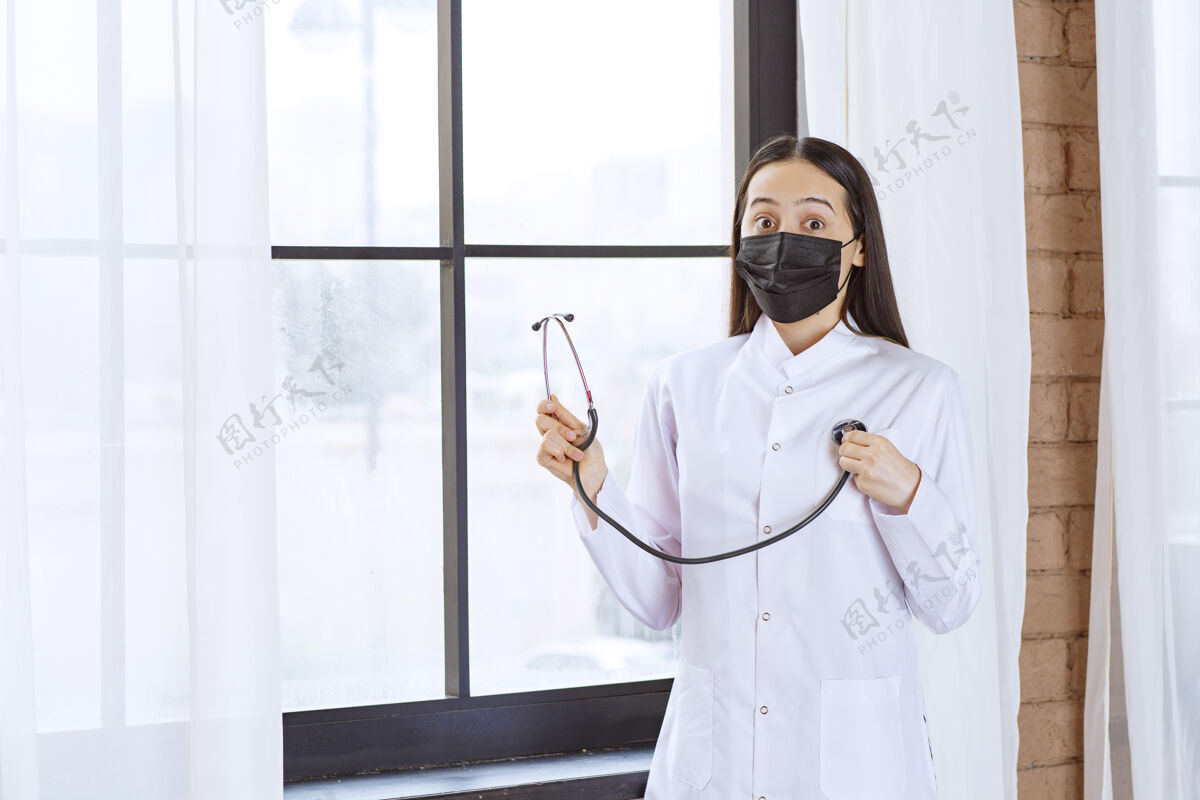 检查戴着黑色口罩的医生站在窗边用听诊器检查心跳感染妇女诊所