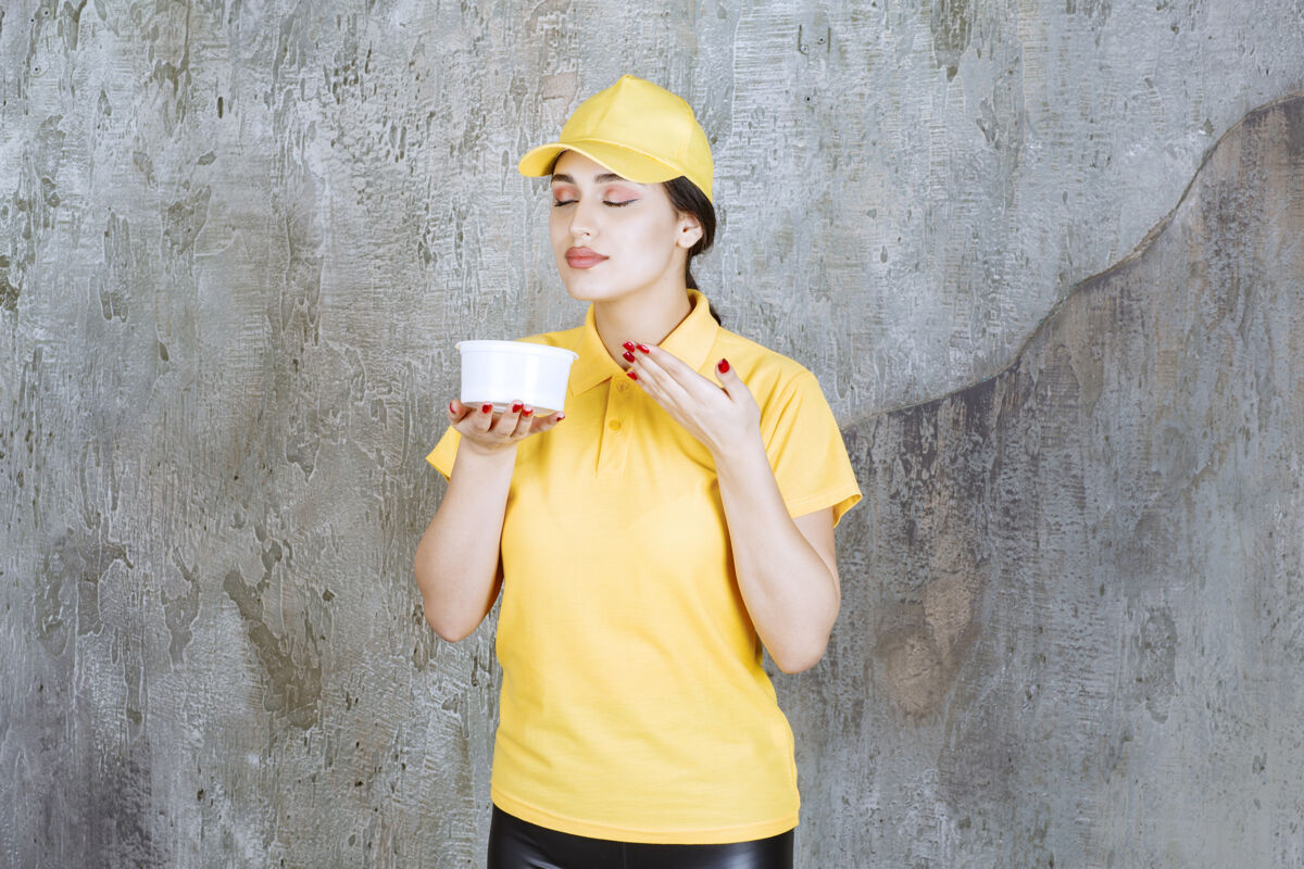 成人穿着黄色制服的女快递员手里拿着一个外卖杯 闻着产品的味道味道职员年轻人