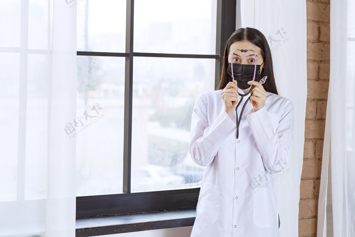 医疗戴着黑色口罩的医生站在窗边 带着听诊器设备感染制服