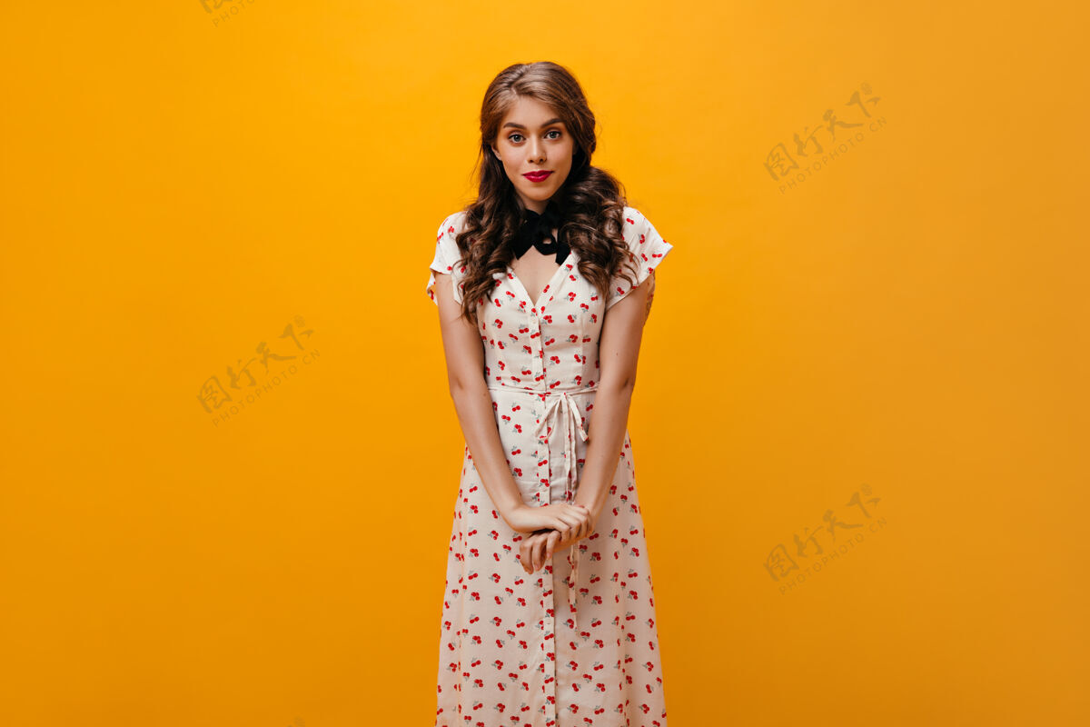 成人害羞的女士穿着印花裙在橙色背景上摆姿势漂亮的年轻女孩穿着时髦的衣服看着镜头微笑橙色表情