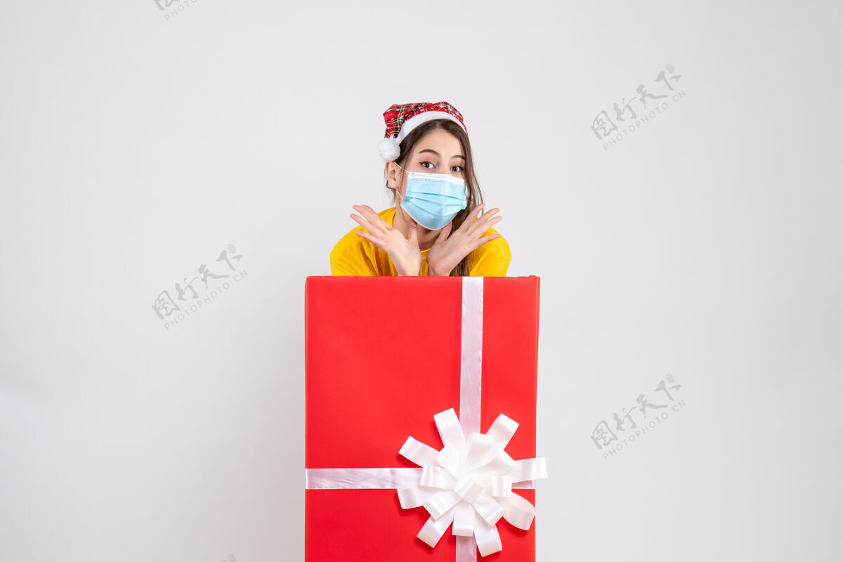 节日前视图可爱的女孩戴着圣诞帽和面具站在大圣诞礼物后面盒子圣诞节惊喜