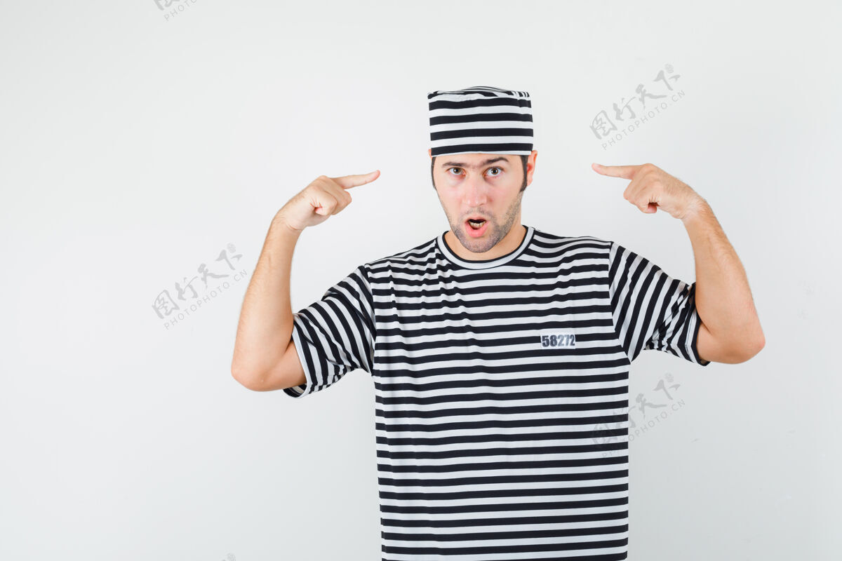 胡须年轻男子指着自己头上的t恤衫 戴着帽子 看上去很自信 前视图自信肖像脸