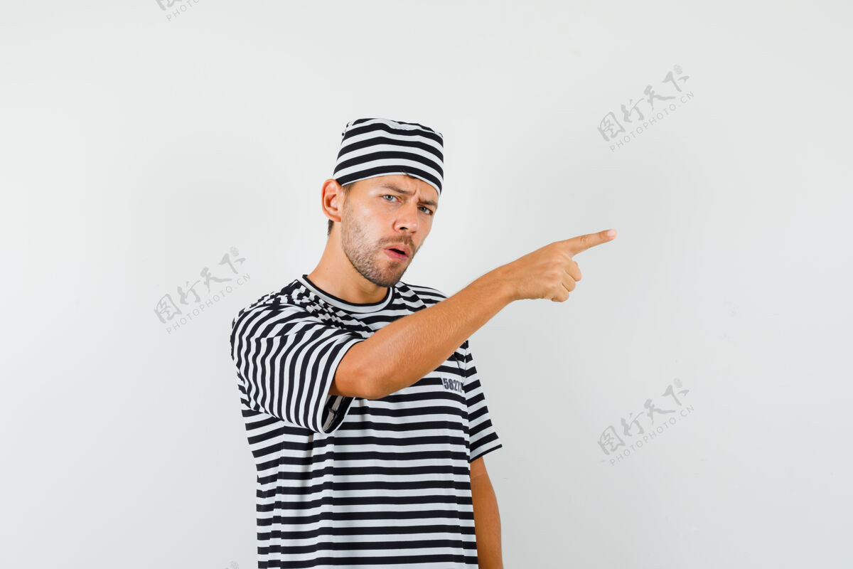 现代一个戴着条纹t恤帽子的年轻人指着别处 满脸疑惑手指衬衫离开