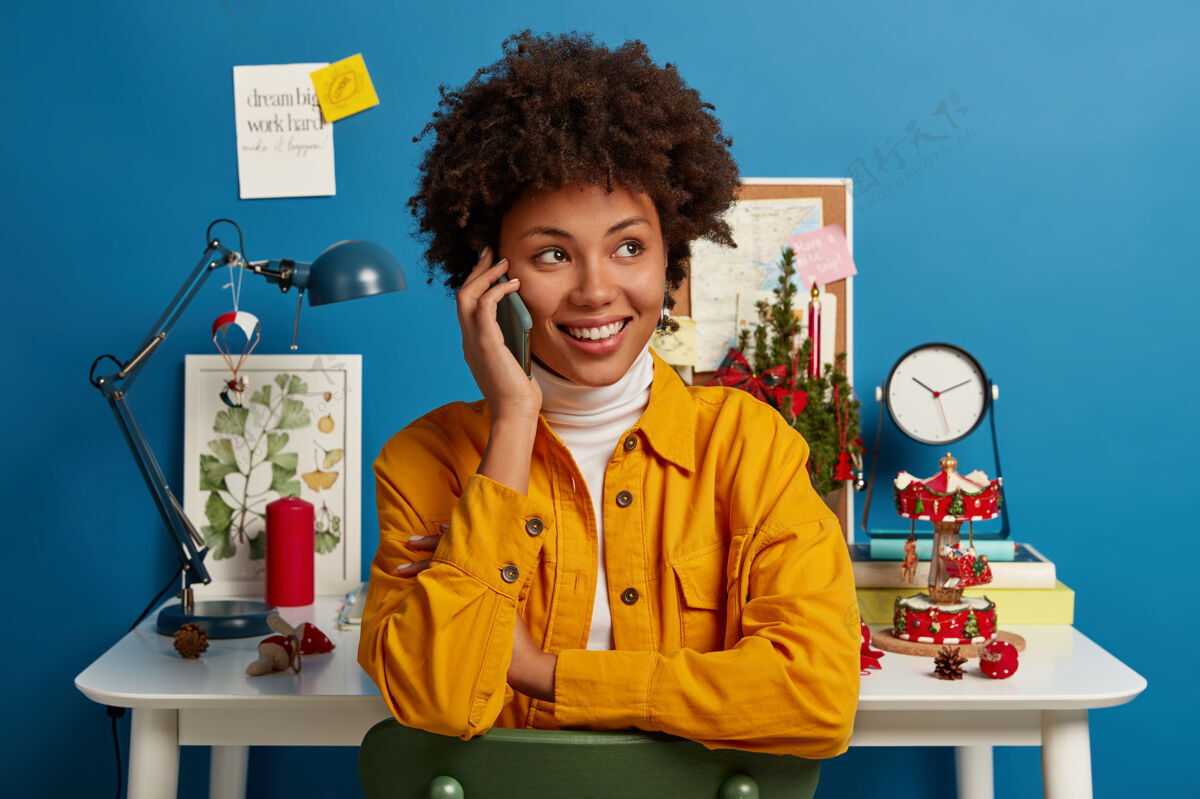 说话快乐成功的美国黑人女企业家有电话交谈 通过智能手机与同事讨论计划 在家做自由职业者 微笑着看别处 在室内桌面附近摆姿势积极分享当代