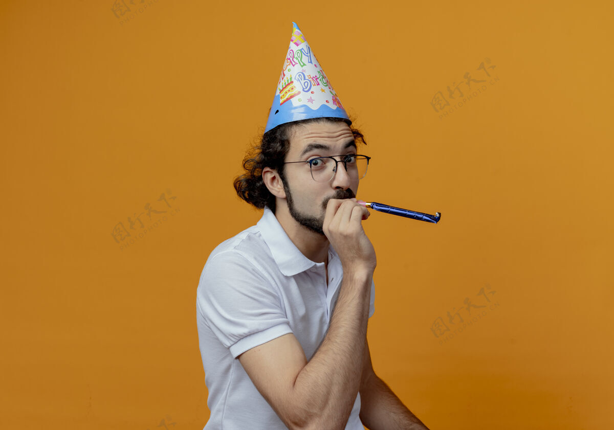 口哨高兴的帅哥戴着眼镜和生日帽吹着哨子隔离在橙色的背景上眼镜戴帅哥