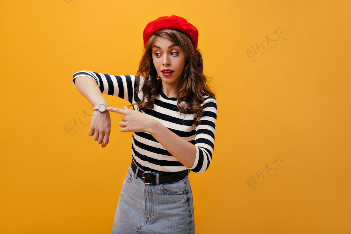 肖像一位戴着红色贝雷帽的女士惊讶地指着我看可爱的年轻女子 嘴唇明亮 戴着漂亮的帽子 在橙色的背景下摆姿势衬衫年轻女性