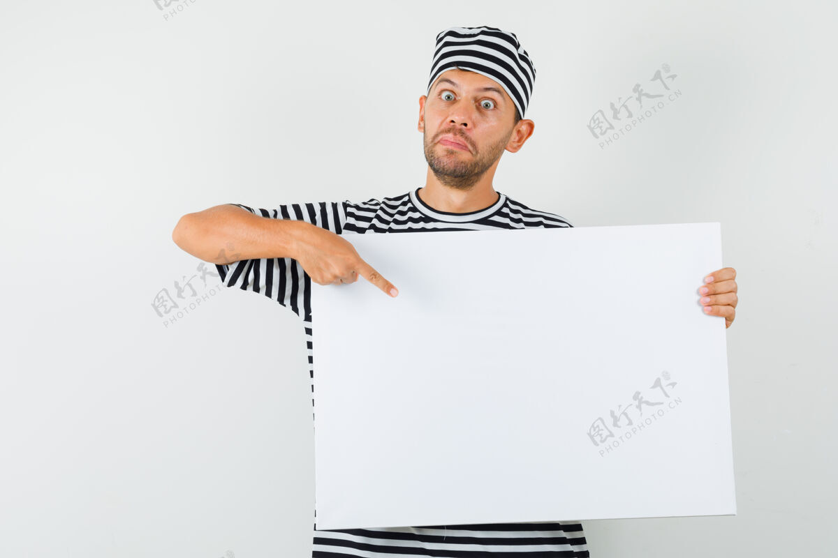 帆布一个年轻人指着一块空白的帆布 戴着条纹t恤帽子 看上去很惊讶胡茬男衬衫