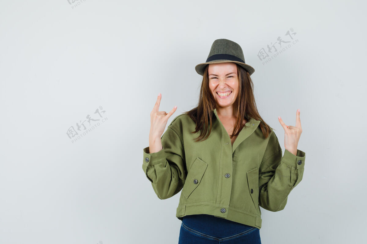 时尚年轻的女士在夹克裤子帽子做摇滚符号和看起来快乐女士帽子裤子