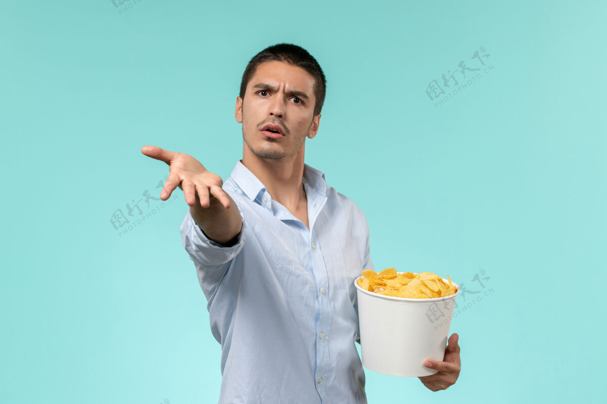 电影正面图年轻人拿着篮子和土豆在蓝墙上吃着看电影孤独的遥远的电影院年轻人男人成人