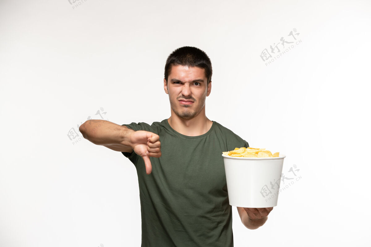 视图正面图身穿绿色t恤的年轻男性手持土豆cips 在白墙上显示不同的标志孤独的电影人成人电影肖像