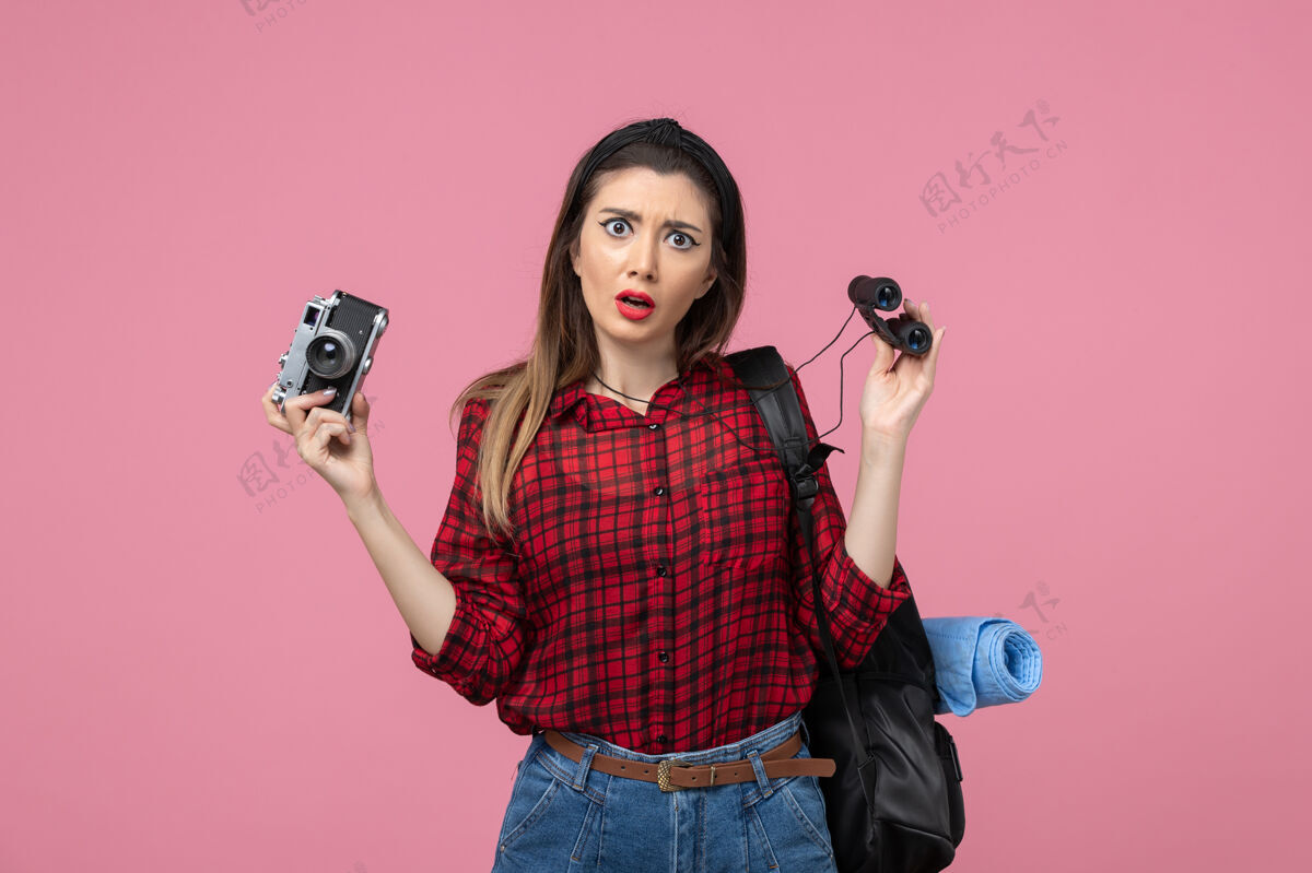 脸前视图年轻女性用双筒望远镜和相机对粉红色背景色的女人人类漂亮望远镜电话