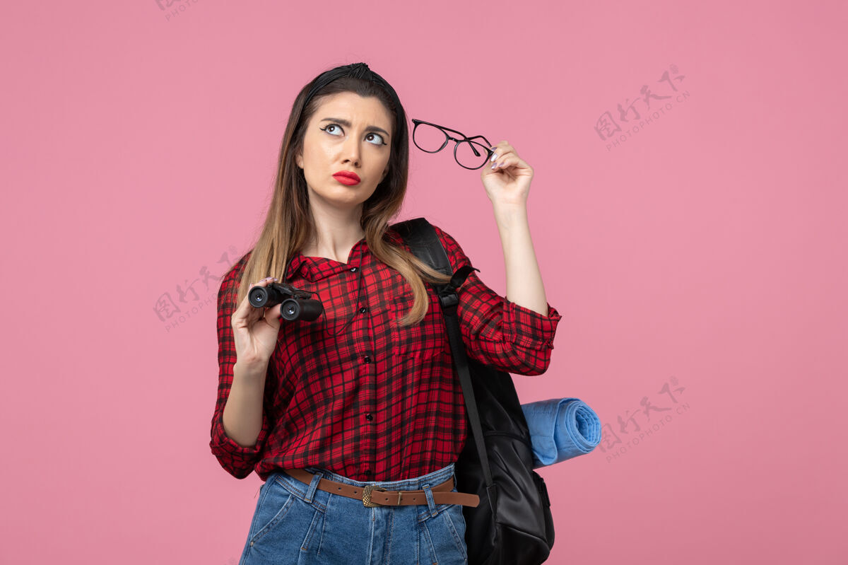 年轻女性正面图穿红色衬衫的年轻女性用双筒望远镜在粉色背景上做女人色模特衬衫黑发女士