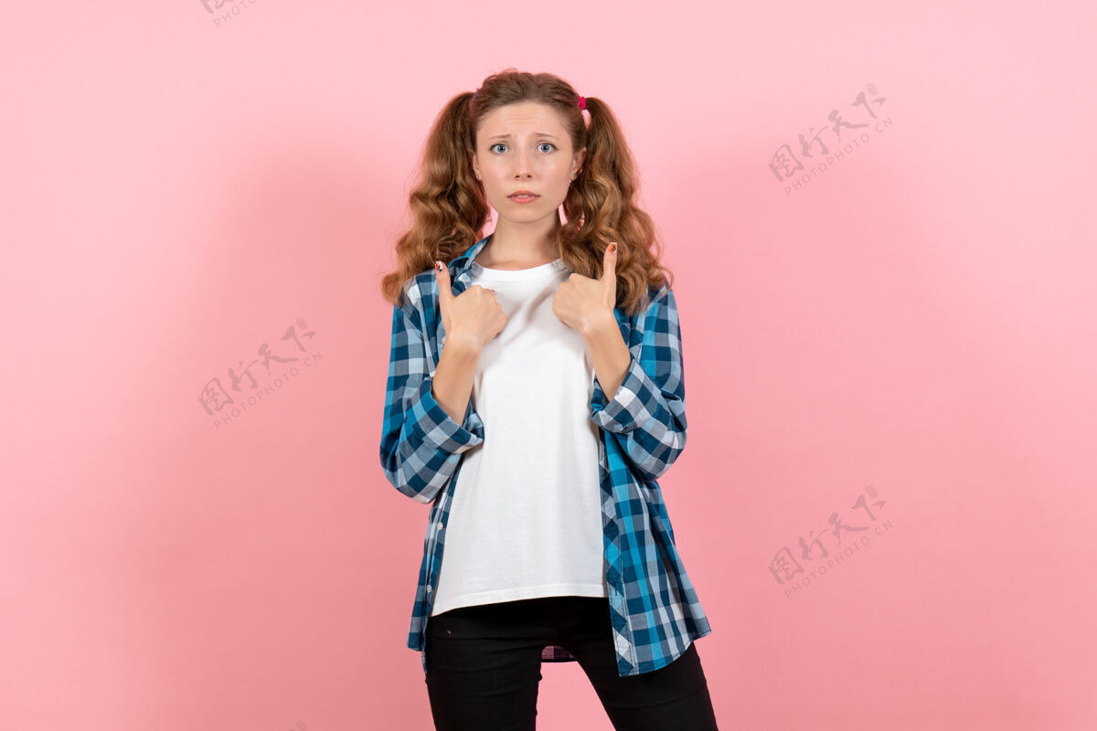 漂亮正面图：穿着格子衬衫的年轻女性在粉色背景上摆姿势模特儿情感童男少女肖像姿势衬衫