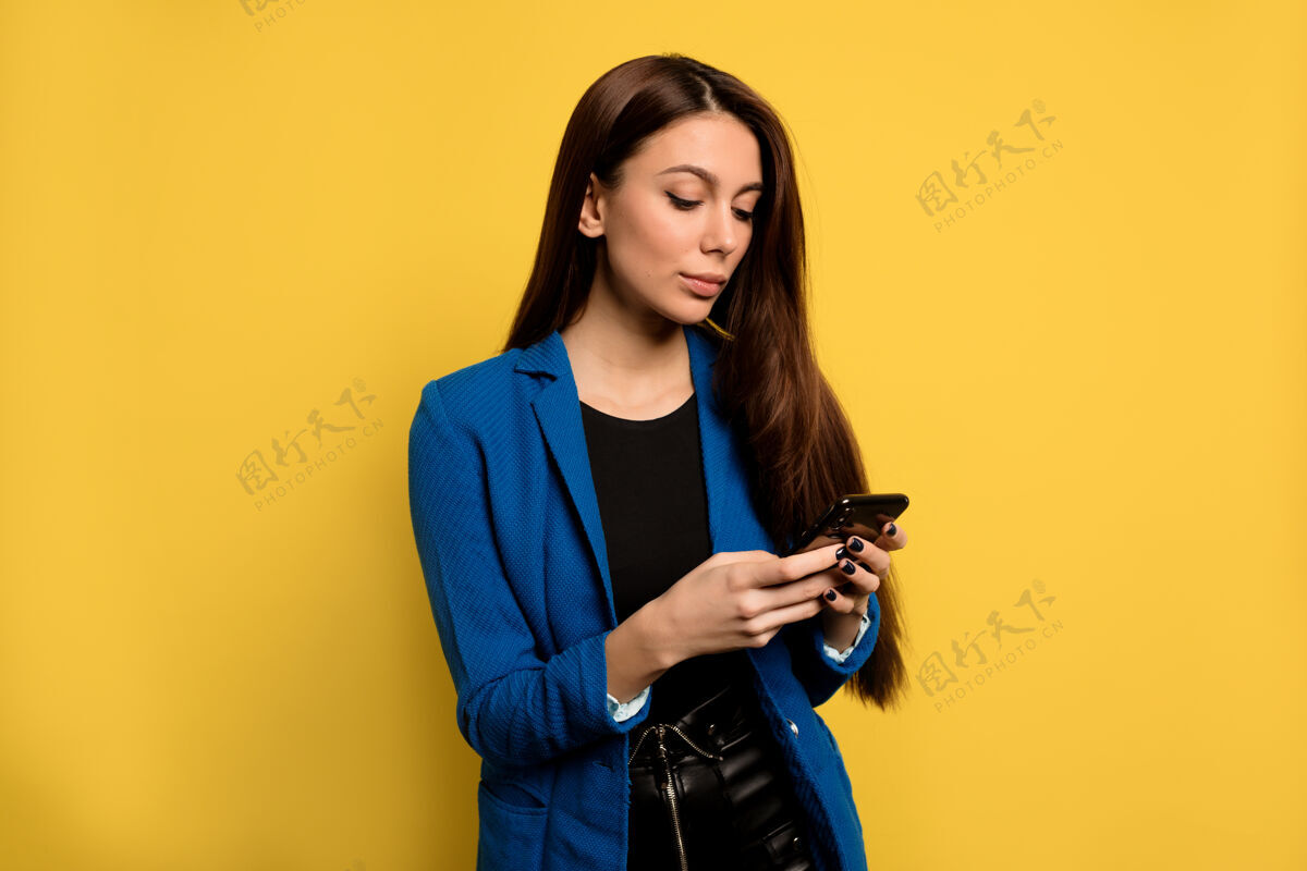 指向忙碌时尚的商务女性 深色长发 隔着隔离墙使用智能手机欧洲女性在黄色墙上滚动手机侧线年轻积极