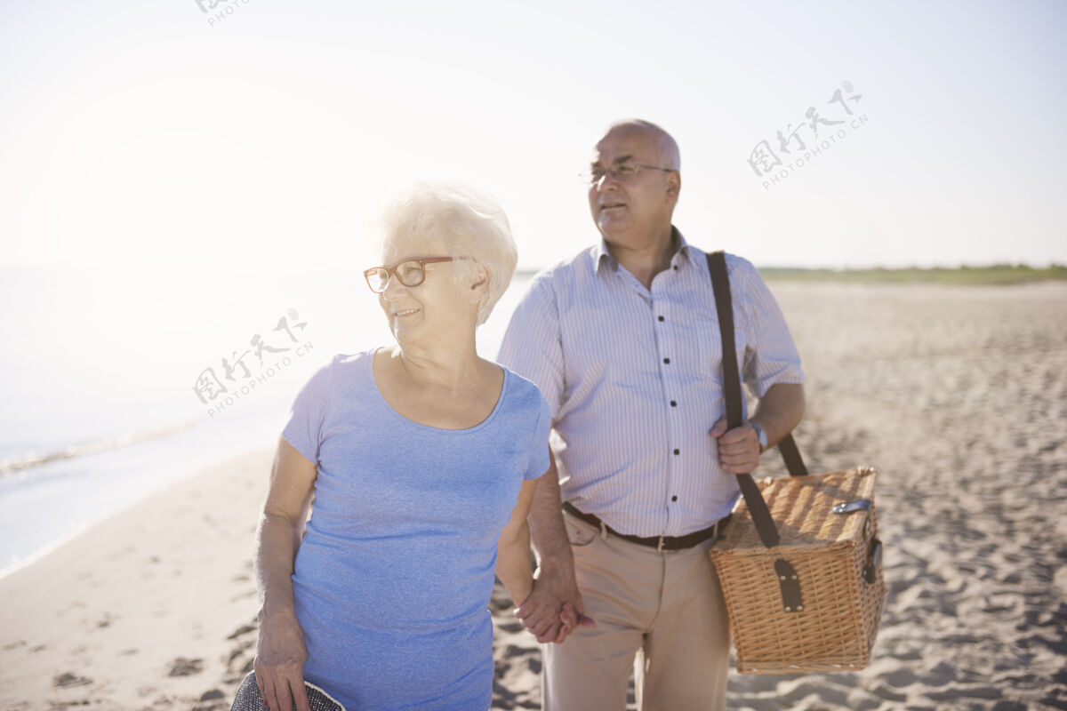 假日寻找一个完美的地方野餐老年夫妇在海滩 退休和暑假的概念日落牵手散步