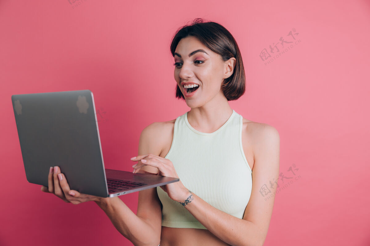 工作粉色背景的女人张着嘴拿着笔记本电脑使用欢呼成人