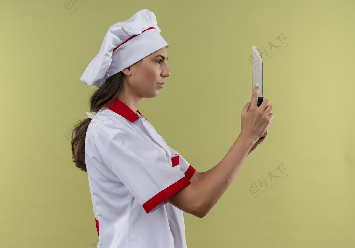 侧身身着厨师制服的年轻自信的白人厨师女孩站在一边 拿着一把刀放在绿色的地方 留着复印空间女孩复制立场