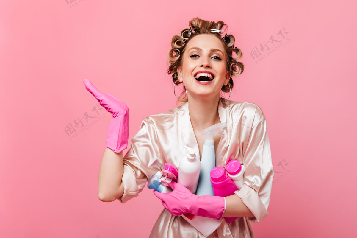 年轻穿着粉红色长袍的女人笑着把洗衣粉放在隔离的墙上人快乐家庭主妇