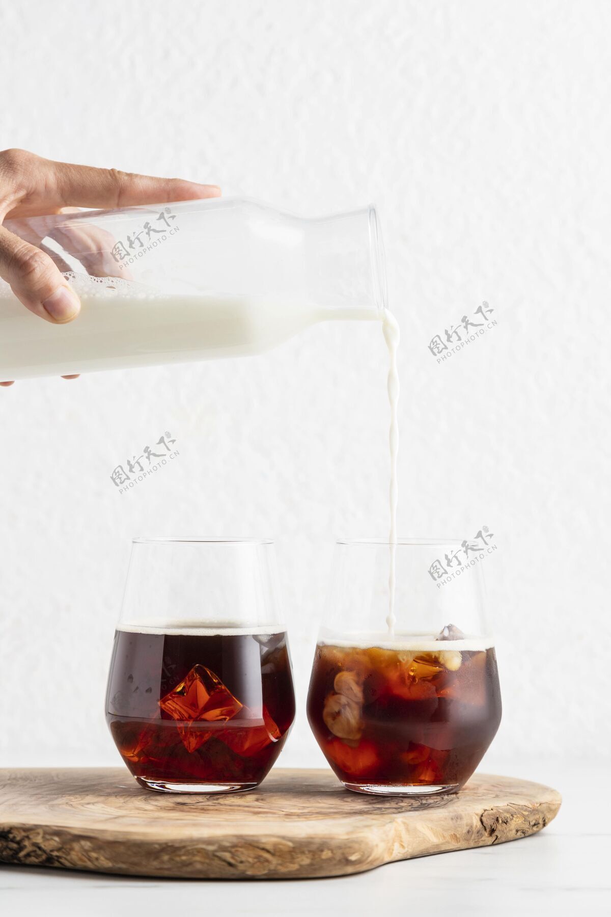 冰在咖啡杯里手倒牛奶的正面图纯净透明牛奶