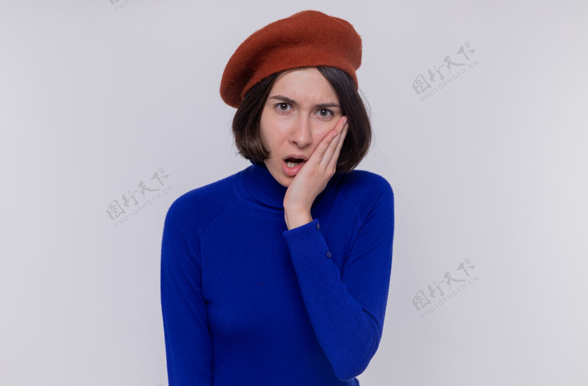 盖一个穿着蓝色高领毛衣 头戴贝雷帽 留着短发的年轻女子看着前面 被吓得捂着嘴站在白色的墙上短裤贝雷帽高领毛衣