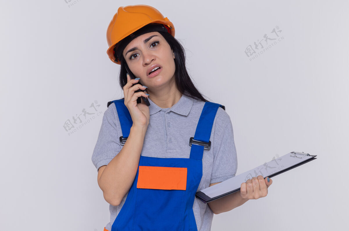 困惑穿着施工制服和安全帽的年轻建筑工人年轻手机建筑商