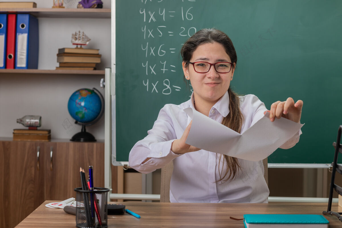 女人年轻的女老师戴着眼镜撕着一张纸坐着看着不悦年轻人学校老师