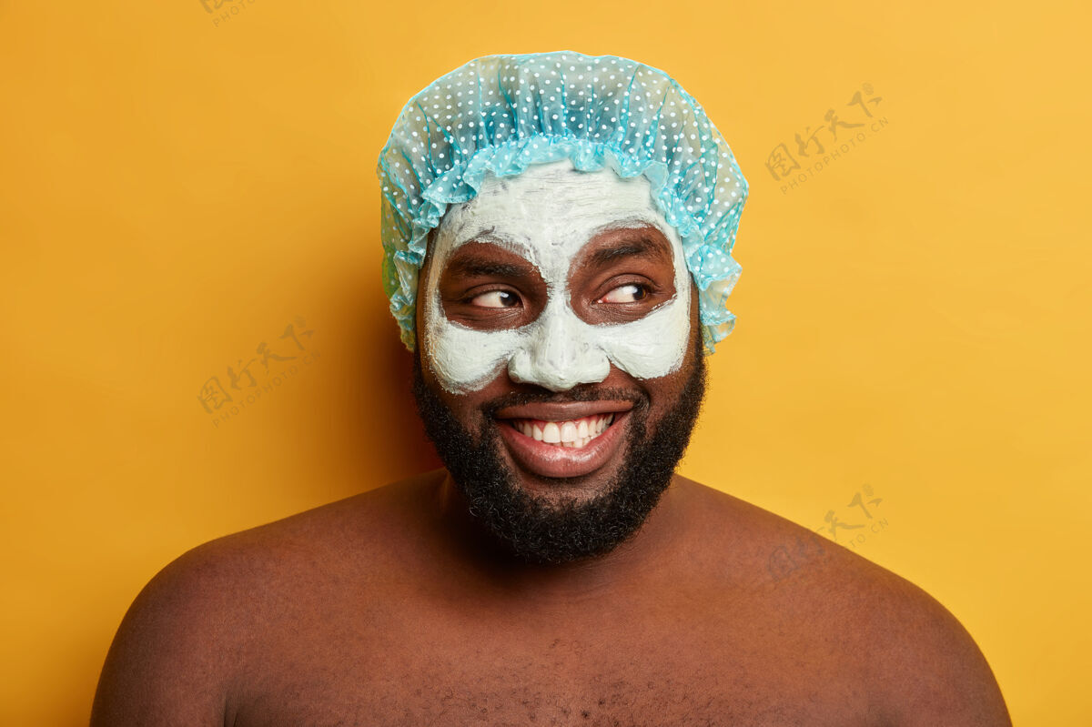 柔软快乐黑皮肤男人的特写肖像戴浴帽 涂化妆泥面膜涂抹站立皮肤科