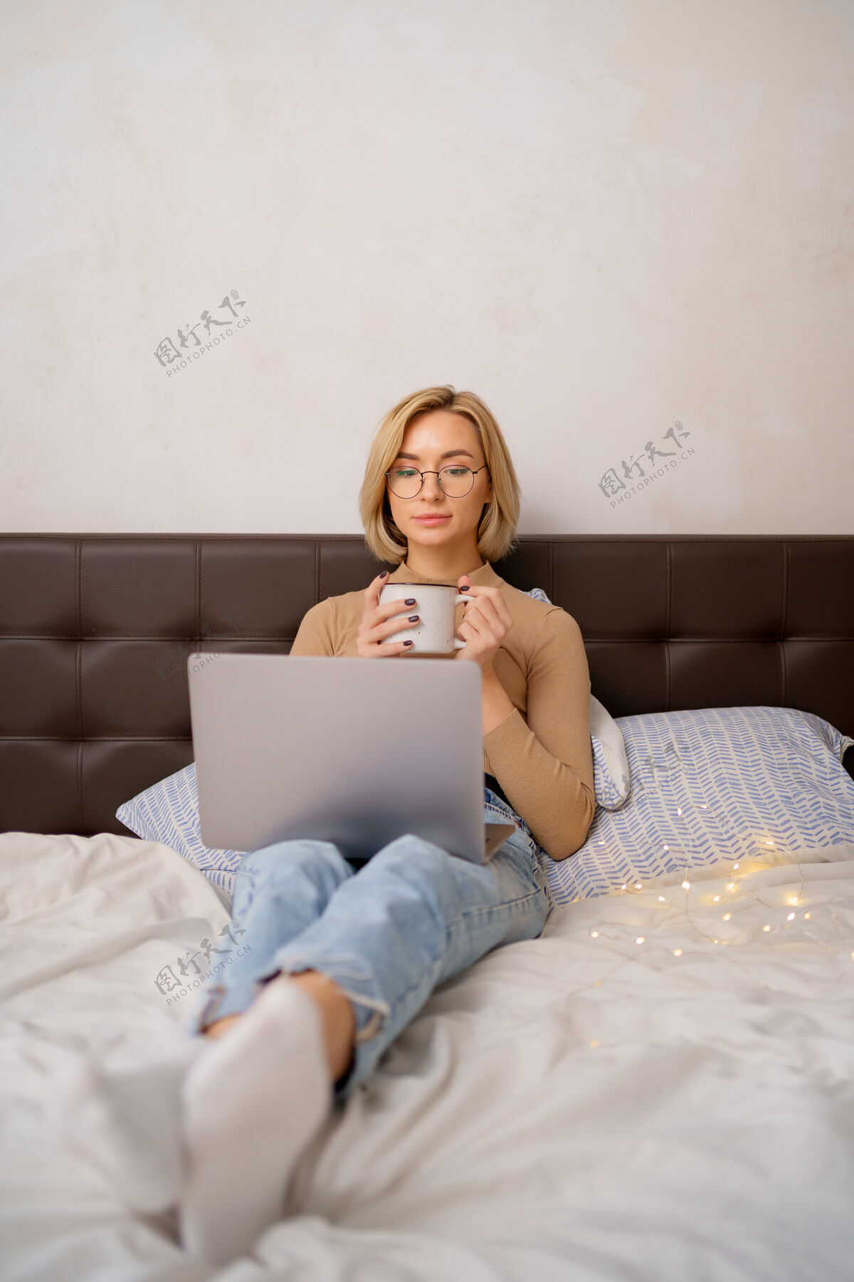 在线女人在卧室里用笔记本电脑放松 喝一杯热咖啡或茶女人卧室打字