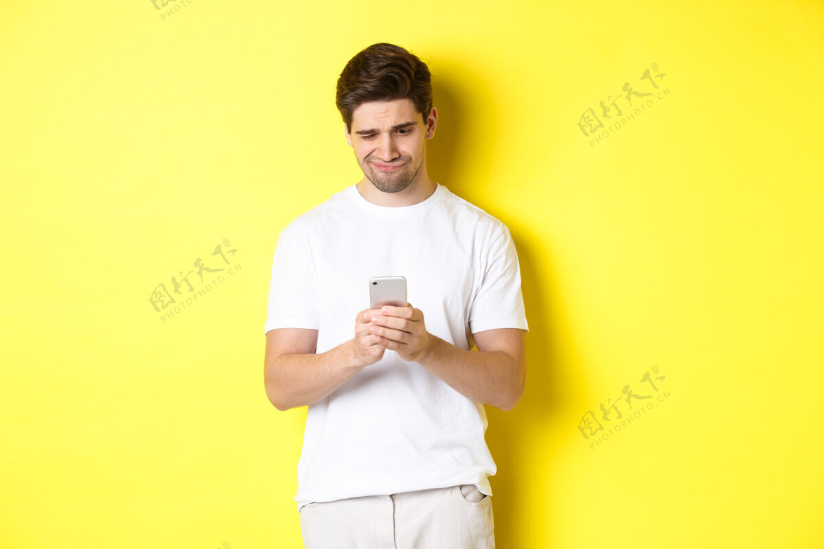 黄色那个家伙不高兴地看着智能手机屏幕 读着手机上奇怪的信息 站在白色t年轻移动时尚