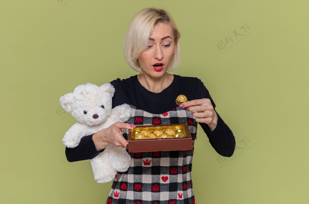 礼物一个穿着漂亮衣服 抱着泰迪熊的快乐而惊讶的年轻女人庆祝巧克力衣服