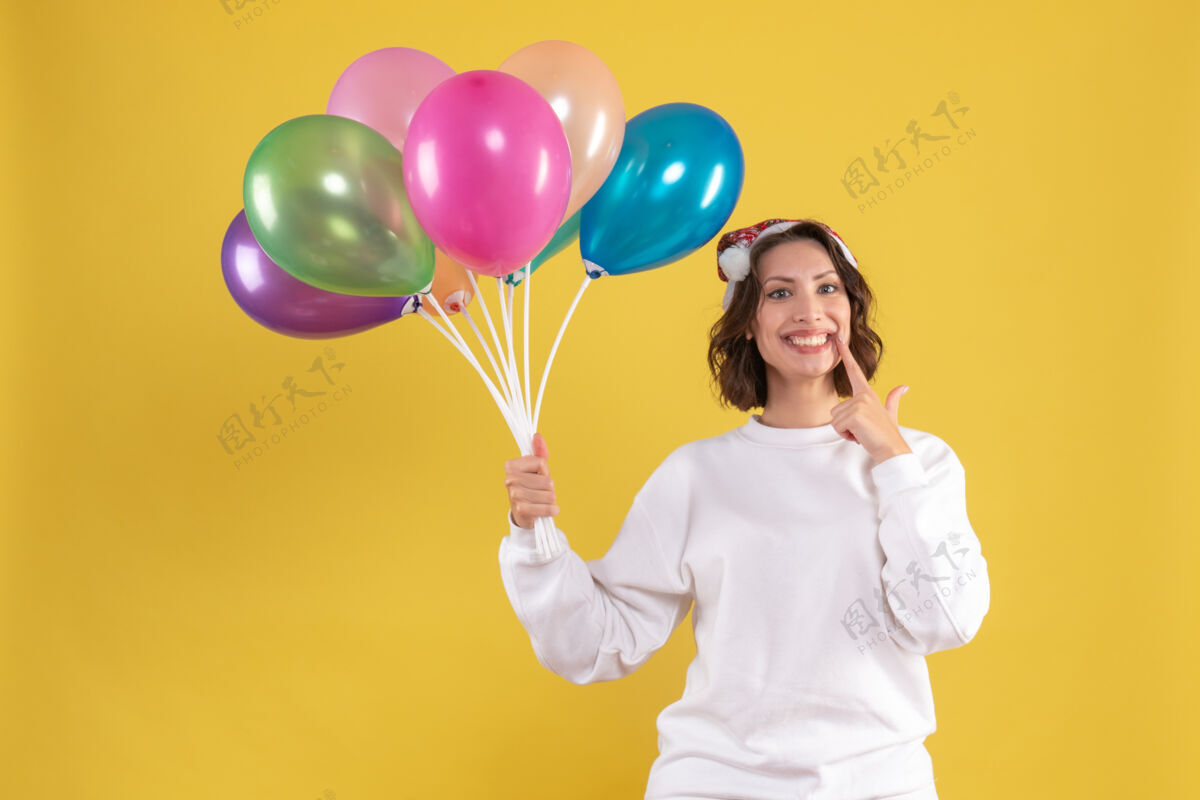 颜色正面图年轻漂亮的女人拿着气球站在黄色的桌子上圣诞新年彩女感慨正面空气气球