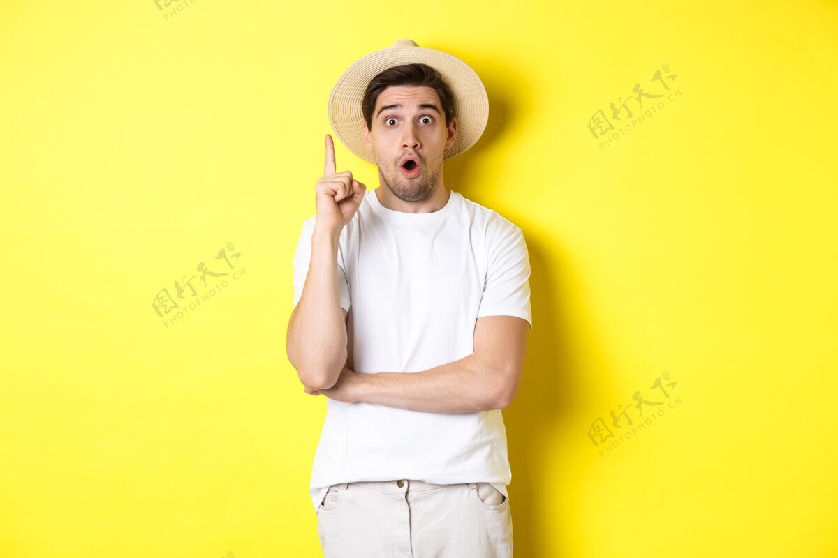 男人戴草帽的年轻人的肖像 有想法 举起手指尤里卡标志 提出建议 站在黄色背景上模特时尚站着
