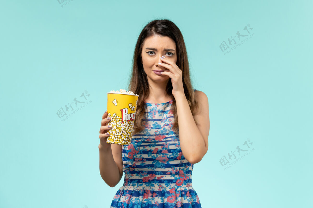 电影正面图年轻女子拿着爆米花包看电影 在蓝色表面哭泣电影院漂亮哭