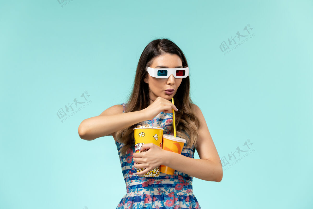 包装正面图年轻女性手持爆米花包 戴着d墨镜在浅蓝色表面喝酒电影电影太阳镜