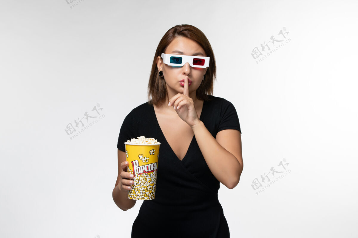 前面正面图：年轻女性戴着d型太阳镜拿着爆米花包 在白色书桌上看电影电影院抱着包装