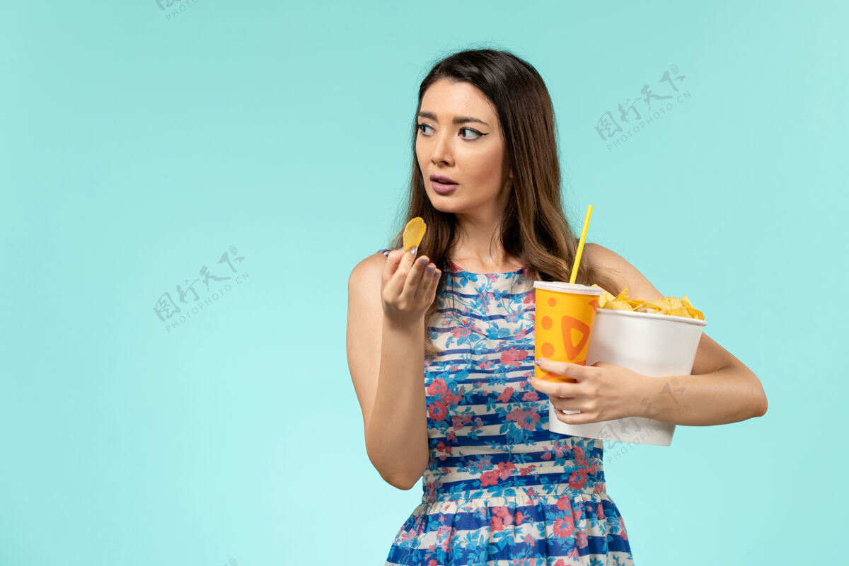 女性正面图年轻的女性拿着篮子和薯片 在浅蓝色的表面上喝水年轻的女性漂亮女士