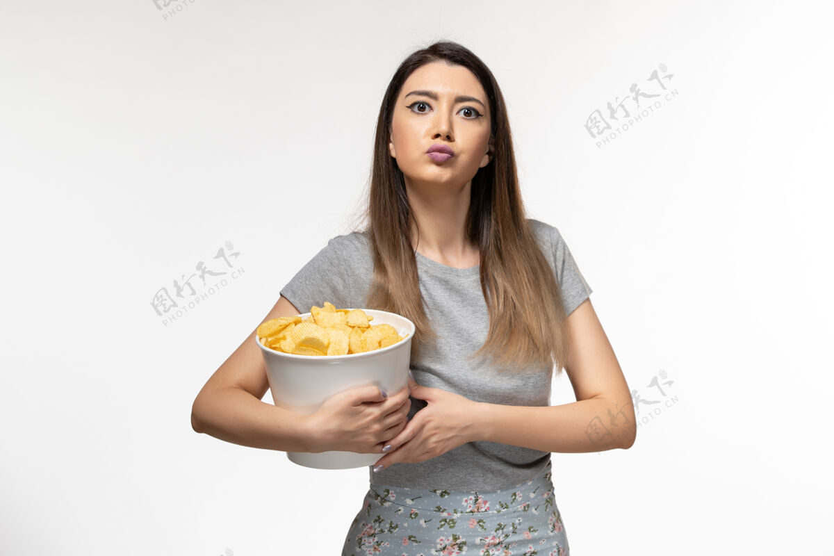 美丽正面图年轻的女性正在吃薯片 在浅白色的表面上看电影观看电影院电影