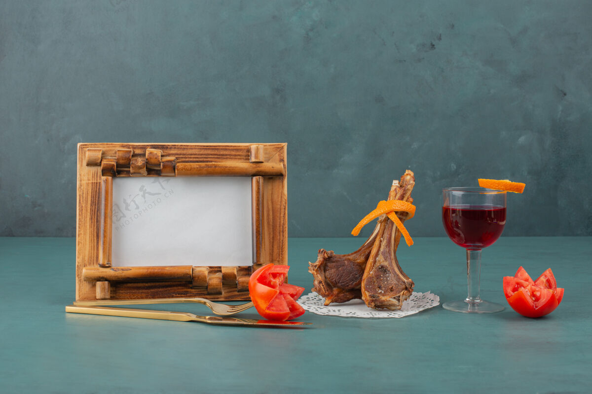 排骨蓝桌上有烤羊排 相框和一杯葡萄酒西红柿切片餐具