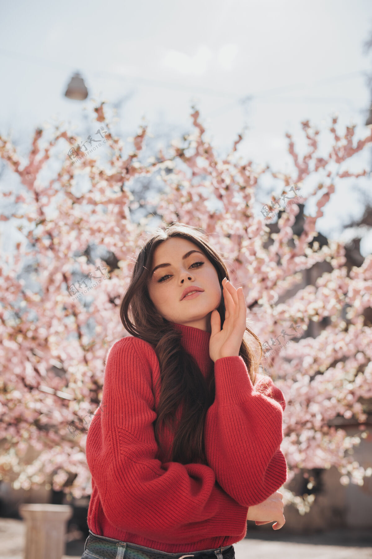 年轻在樱花的背景下 一个穿着鲜艳毛衣的漂亮女人看着镜头一张穿着红色毛衣的女人在外面摆姿势享受春天的快照贝雷帽花芳香