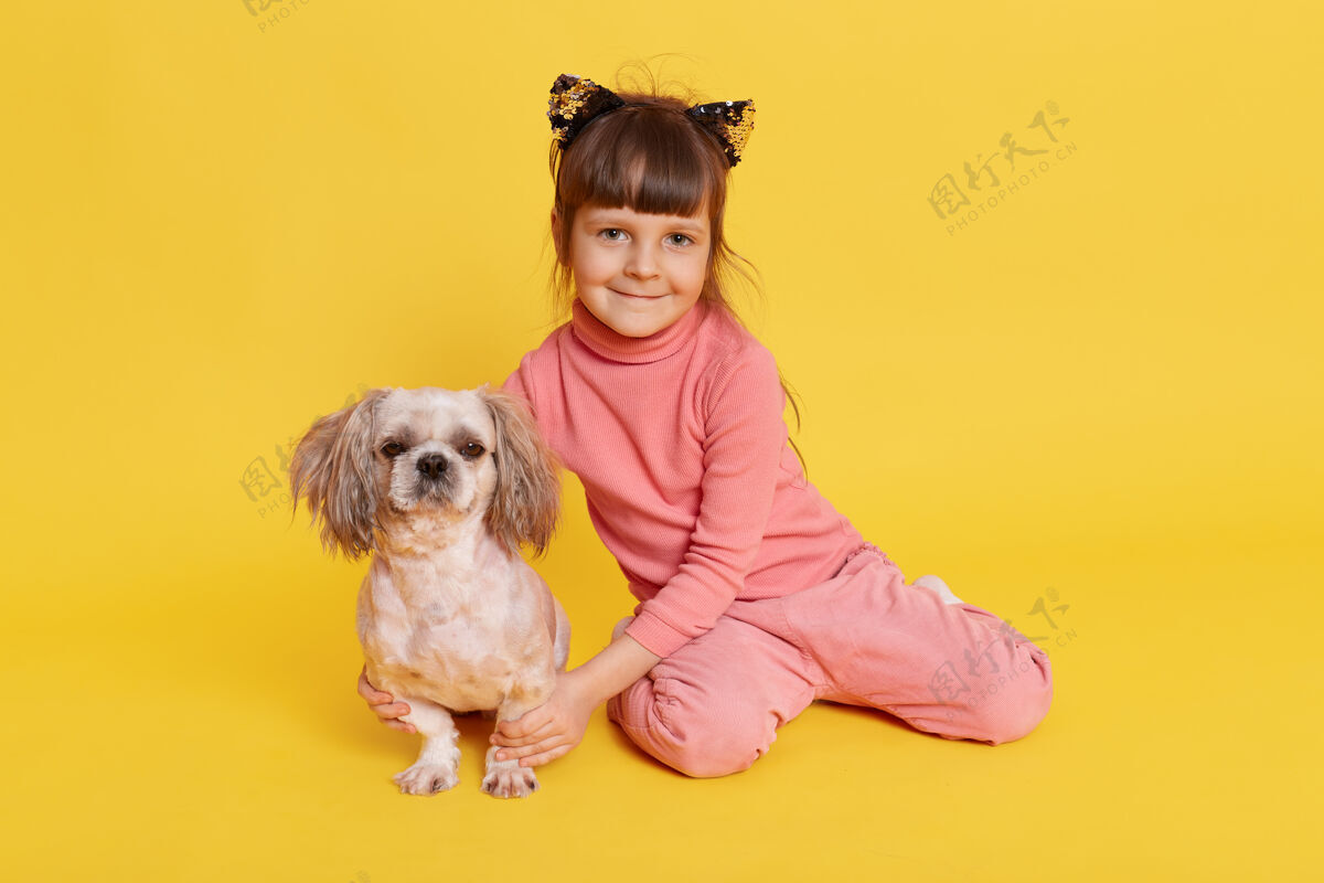 快乐小女孩带着小狗在室内摆姿势 黄色的脸上露出微笑可爱小狗宝贝