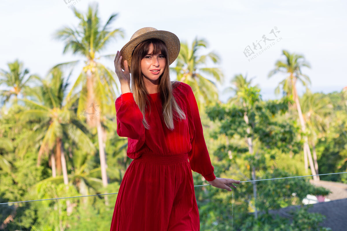 帽子穿着红色夏装 戴着草帽 在阳台上享受热带海景和棕榈树的快乐女人女士休闲夏季