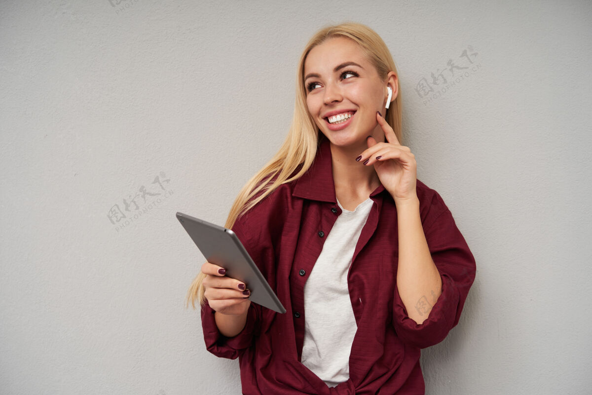 衣服室内照片：一位迷人的年轻女子 一头金色的长发轻轻地抚摸着她的脖子 面带迷人的微笑 身穿紫红色衬衫和浅灰色背景的白色t恤欢呼长女士