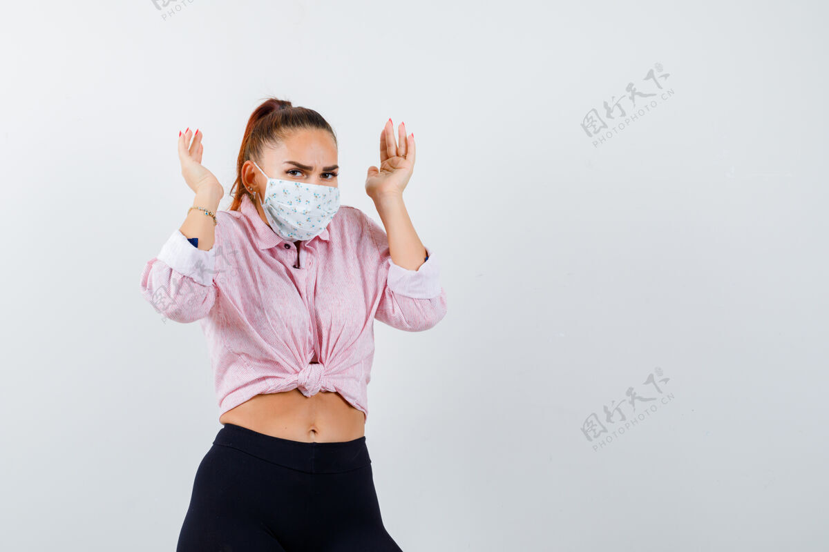 人穿着衬衫 裤子 戴着医用面罩的年轻女性举手靠近头部 看起来很紧张正面图表情商业问题
