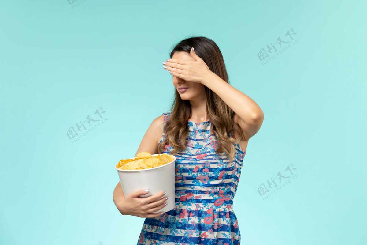 性感正面图：年轻的女性拿着篮子和薯片 在蓝色的水面上看电影电影院前面剧院