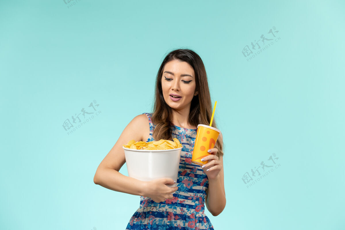 薯片正面图年轻女性拿着篮子和薯片 在蓝色的桌子上喝酒拿着年轻女性剧院