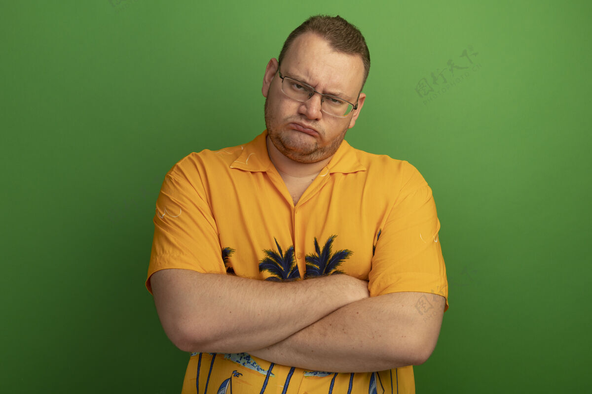 站一个戴着眼镜 穿着橙色衬衫 皱着眉头 双臂交叉的男人站在绿色的墙上男人交叉脸