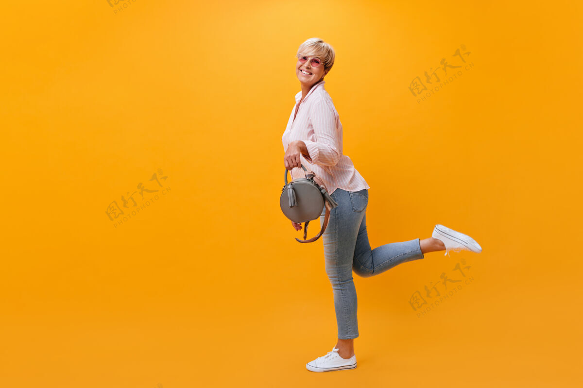 年穿着牛仔裤的快乐女人在橙色背景上玩得很开心短发牛仔裤朋友