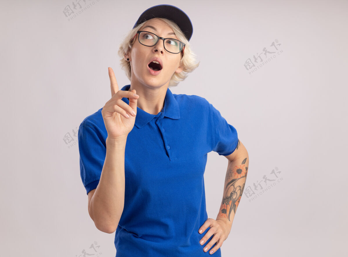 制服身穿蓝色制服 头戴帽子的年轻送货员抬起头 惊讶地用食指指着白墙上站着的东西表演女人目录