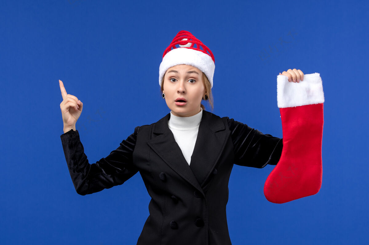 英俊正面图：年轻的女性手拿着红色的圣诞袜在蓝色的墙壁上过年袜子成功执行