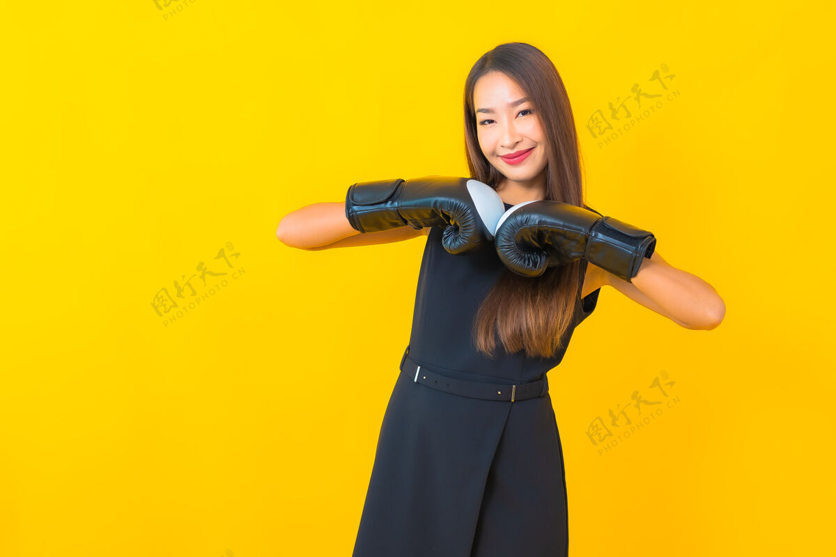 锻炼在黄色背景上画一个戴拳击手套的美丽的亚洲女商人健身冠军肖像
